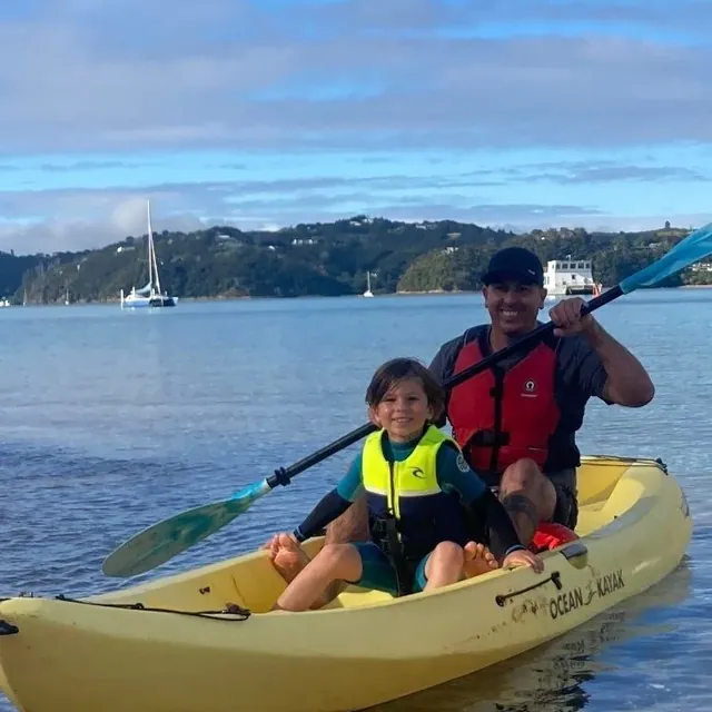 An adult and child smiling in a yellow kayak on the bay