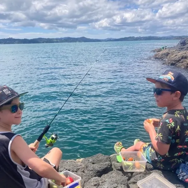 Two children fishing off the rocks beside the bay