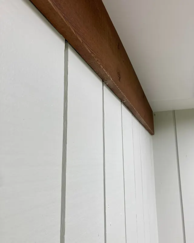 Close-up of white painted wall panelling beneath a stained timber beam